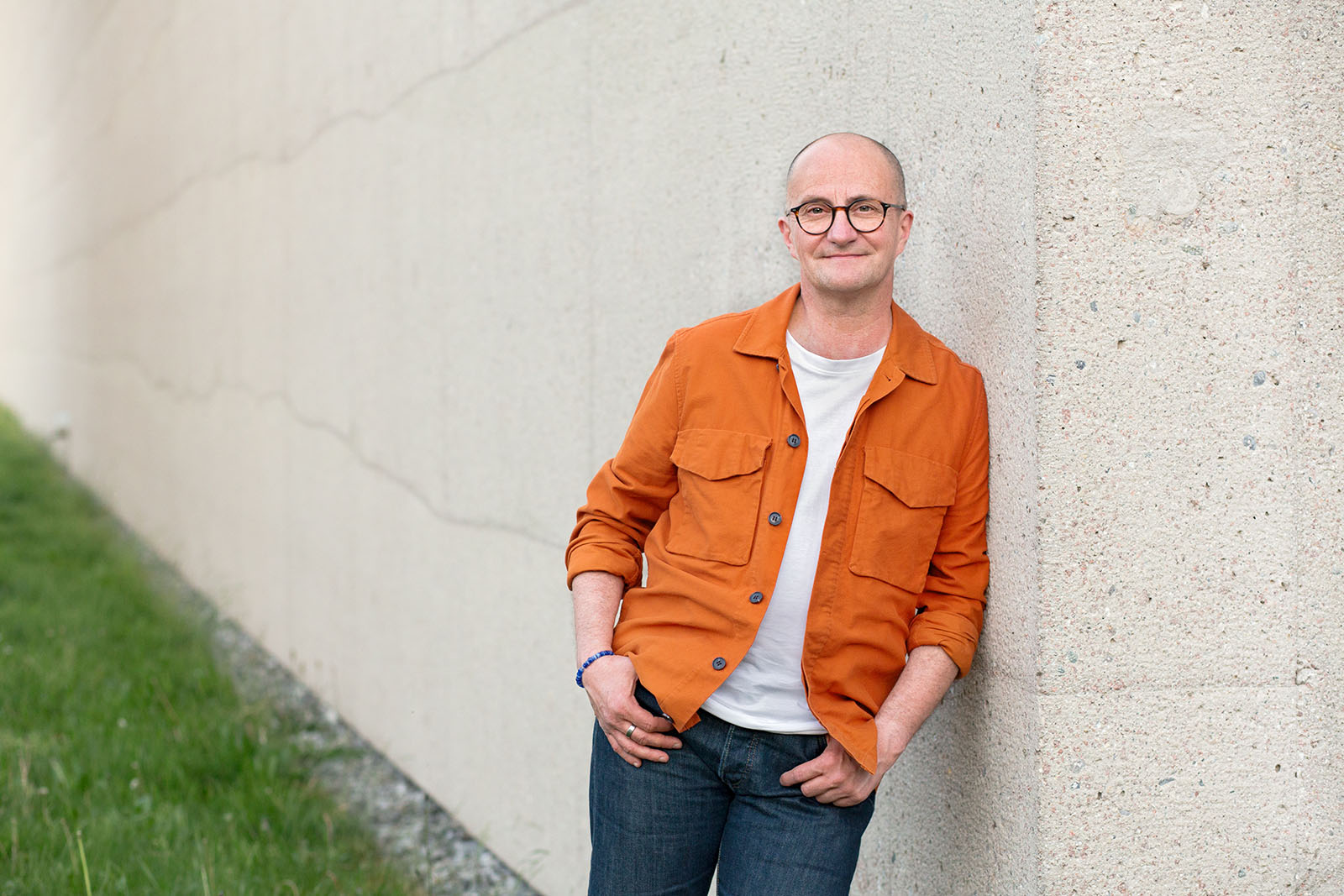 Steven lehnt entspannt mit orangener Jacke an Wand Steven Förster, Chancen-Schritt Coaching ü50, Steven lehnt entspannt mit orangener Jacke an Wand